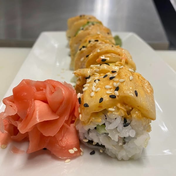 A row of The ChatRoom Restaurant's sushi rolls topped with sauce and sesame seeds, alongside pickled ginger.