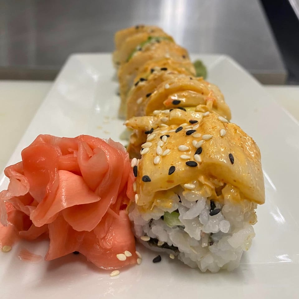 A row of The ChatRoom Restaurant's sushi rolls topped with sauce and sesame seeds, alongside pickled ginger.