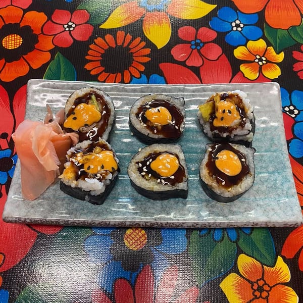 Six pieces of sushi with orange sauce and dark glaze, served with pickled ginger on a blue plate.