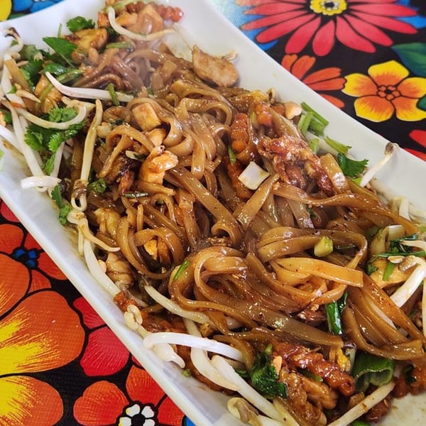 A close-up of The ChatRoom Restaurant's Pad See Ew with wide noodles, chicken, and bean sprouts.