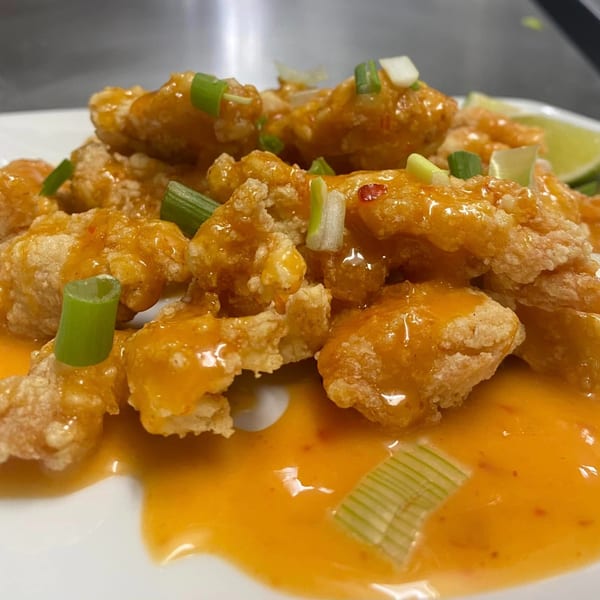 Crispy Asian-fusion chicken or shrimp, coated in orange sauce and garnished with green onions.