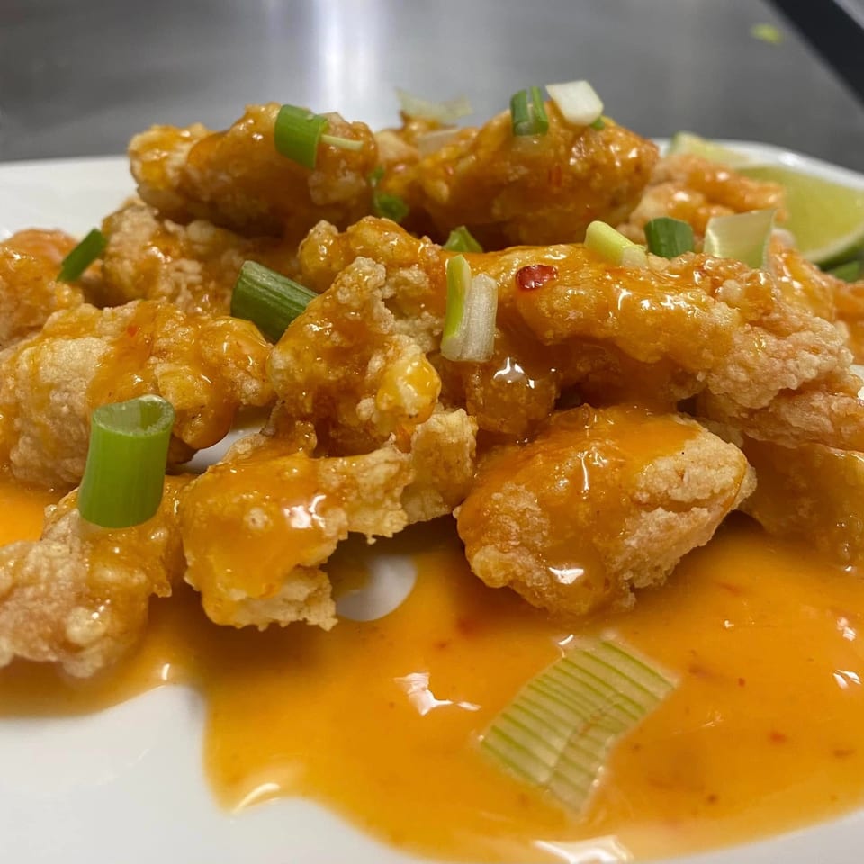 Crispy Asian-fusion chicken or shrimp, coated in orange sauce and garnished with green onions.