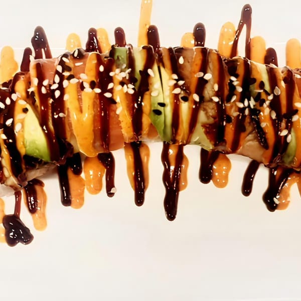 Sushi roll with avocado, fish, sesame seeds, drizzled with dark and orange sauces.